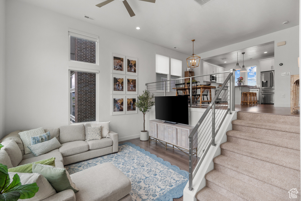 Living room featuring wood finished floors, a chandelier, ceiling fan, stairway, and recessed lighting