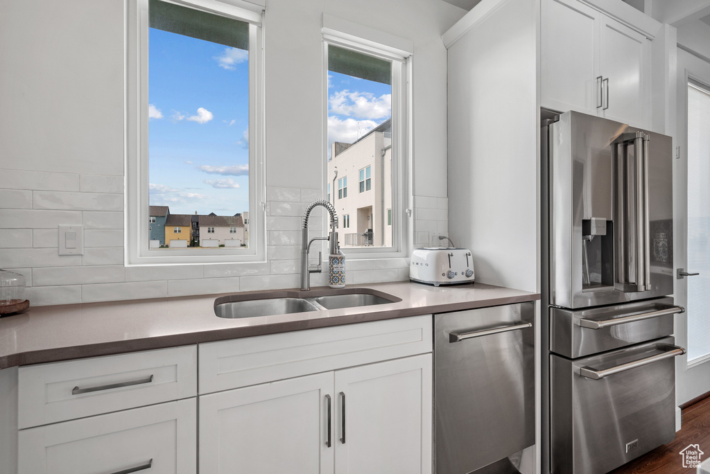 Kitchen featuring appliances with stainless steel finishes, a sink, backsplash, and white cabinets