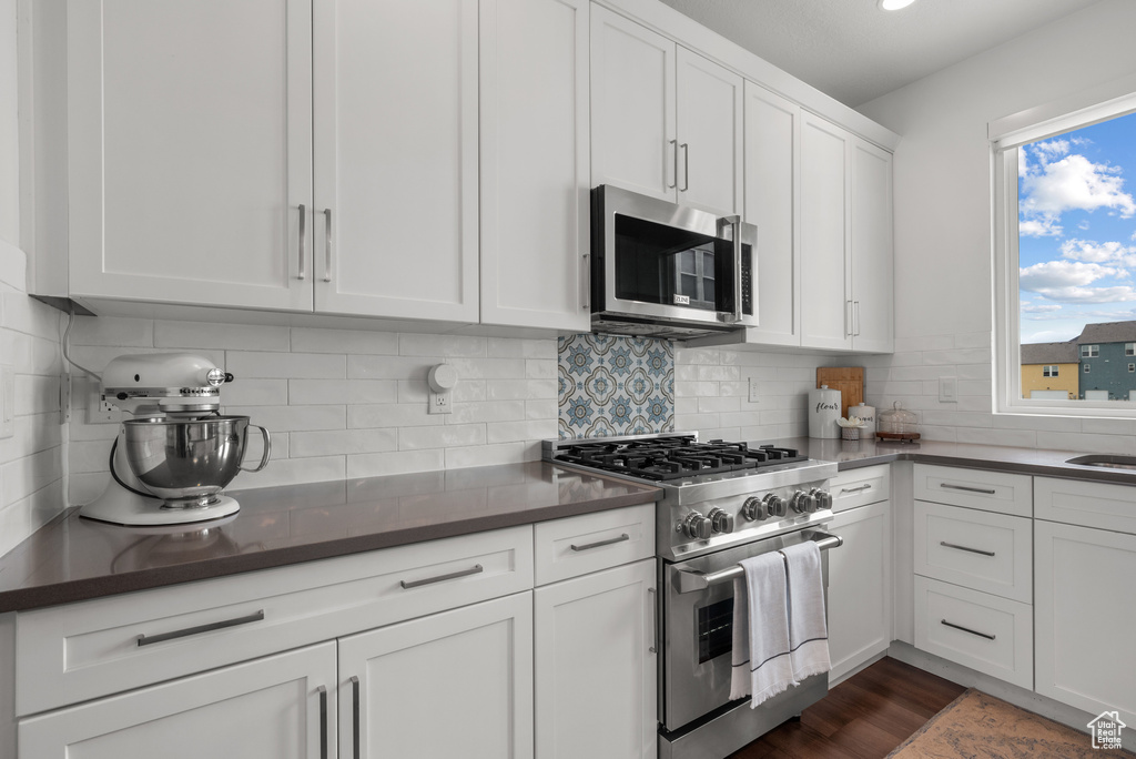 Kitchen with stainless steel appliances, white cabinetry, tasteful backsplash, and dark wood-style flooring