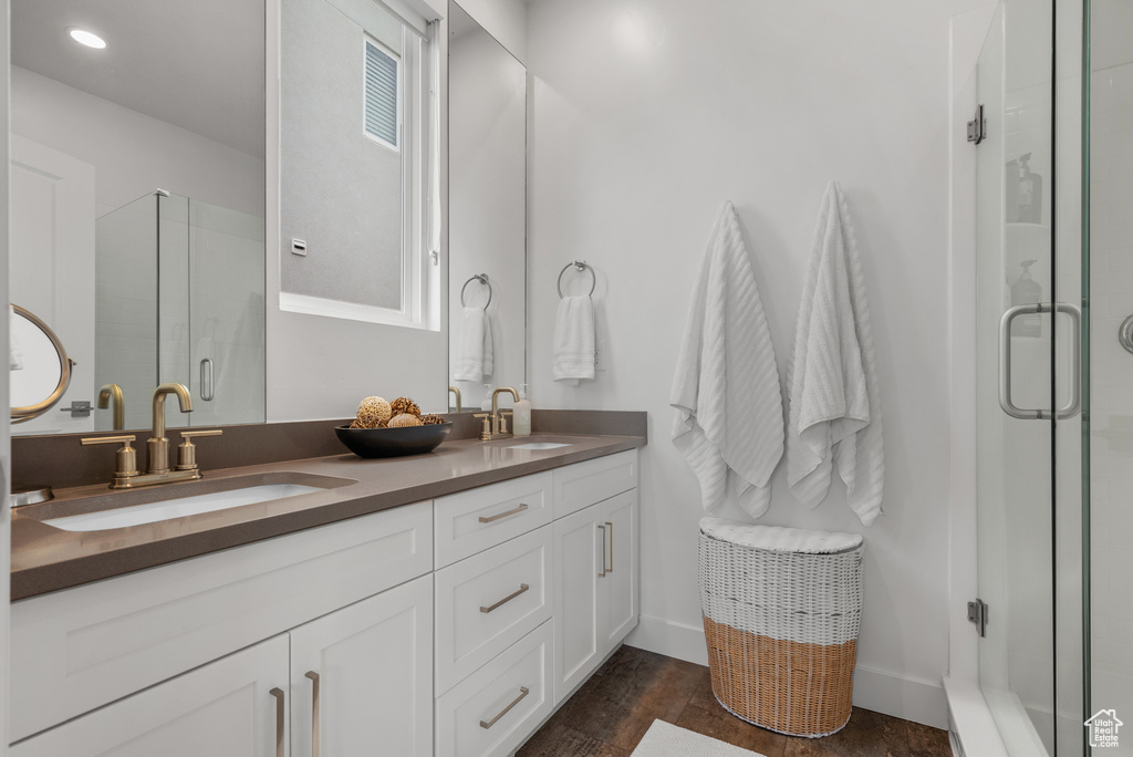 Bathroom featuring a shower stall, double vanity, wood finished floors, and baseboards