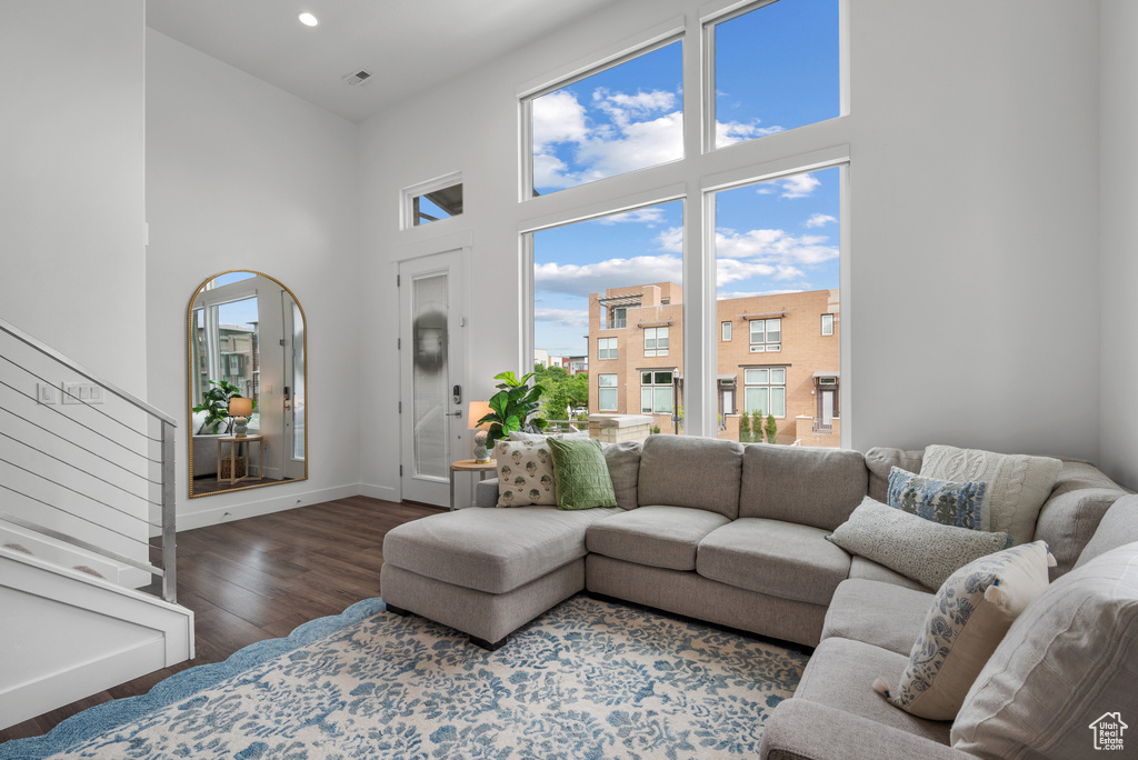 Living area with a towering ceiling, healthy amount of natural light, wood finished floors, baseboards, and stairs