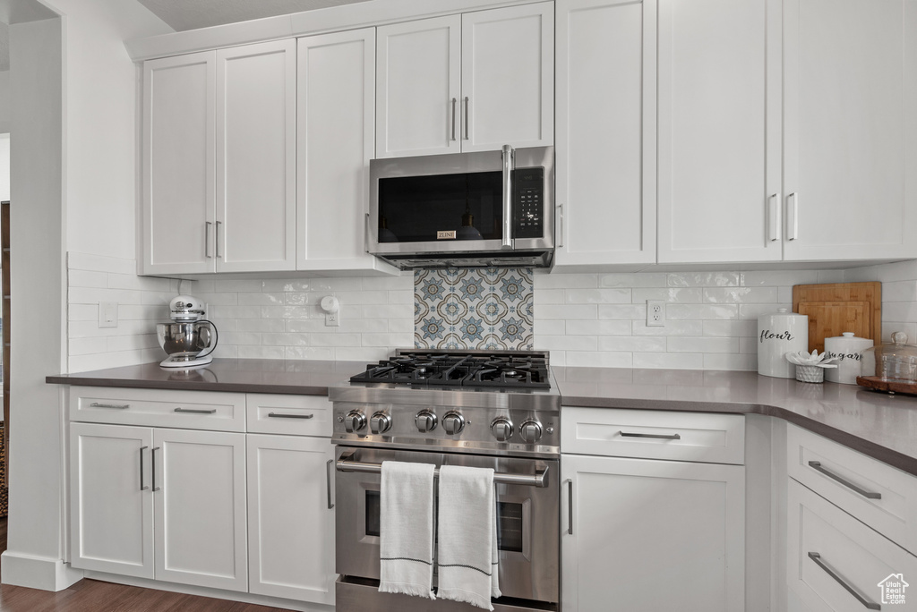 Kitchen featuring stainless steel appliances, white cabinetry, decorative backsplash, and dark countertops
