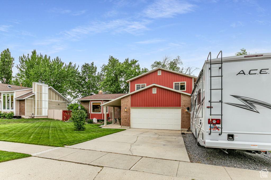 View of front of house with brick siding, a front yard, a garage, driveway, and an outbuilding