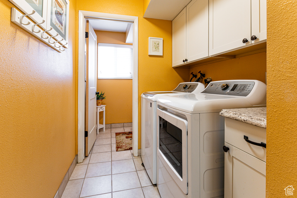 Washroom with cabinet space, separate washer and dryer, light tile patterned floors, and baseboards