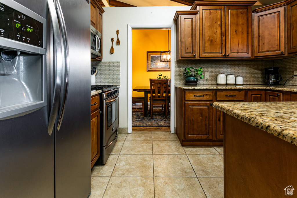 Kitchen featuring appliances with stainless steel finishes, tasteful backsplash, light tile patterned flooring, and light stone counters