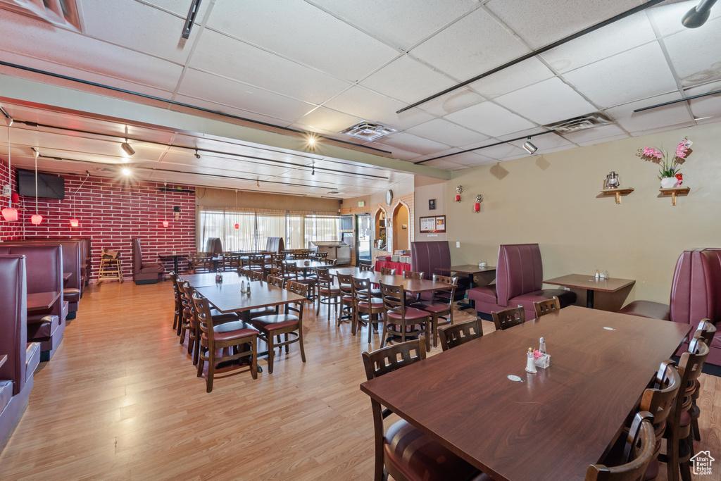 Dining area featuring a paneled ceiling, wood finished floors, and brick wall