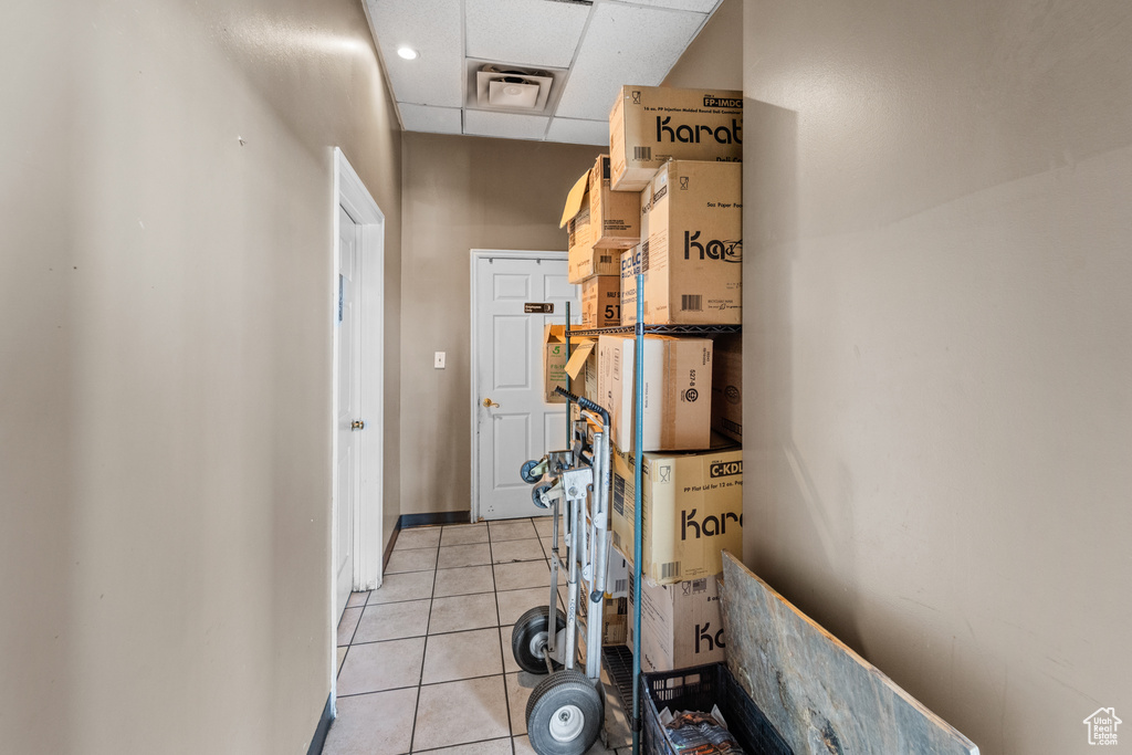 Hallway with light tile patterned floors, a drop ceiling, and baseboards