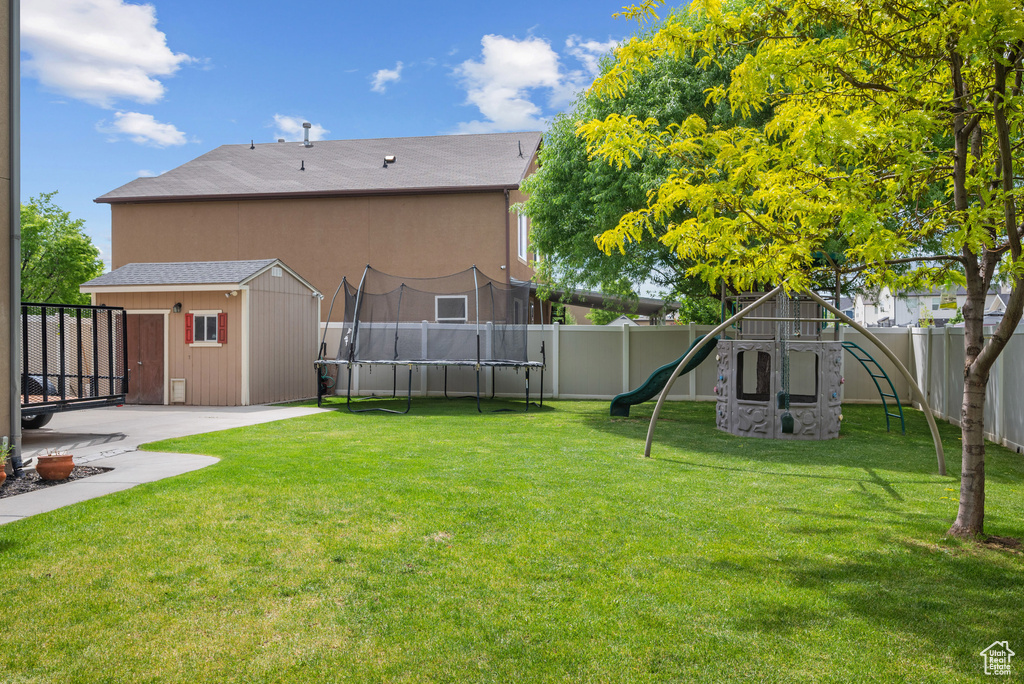 View of yard with a trampoline, a playground, an outdoor structure, a storage unit, and a patio area