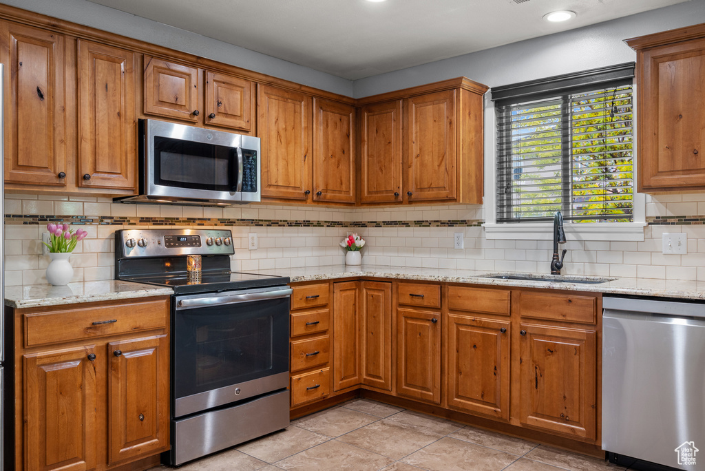 Kitchen featuring appliances with stainless steel finishes, a sink, brown cabinetry, and decorative backsplash