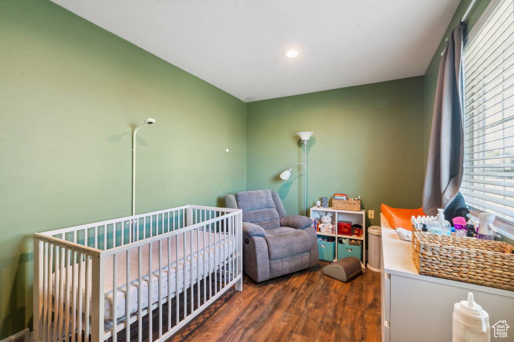 Bedroom with dark wood-type flooring, a crib, and recessed lighting