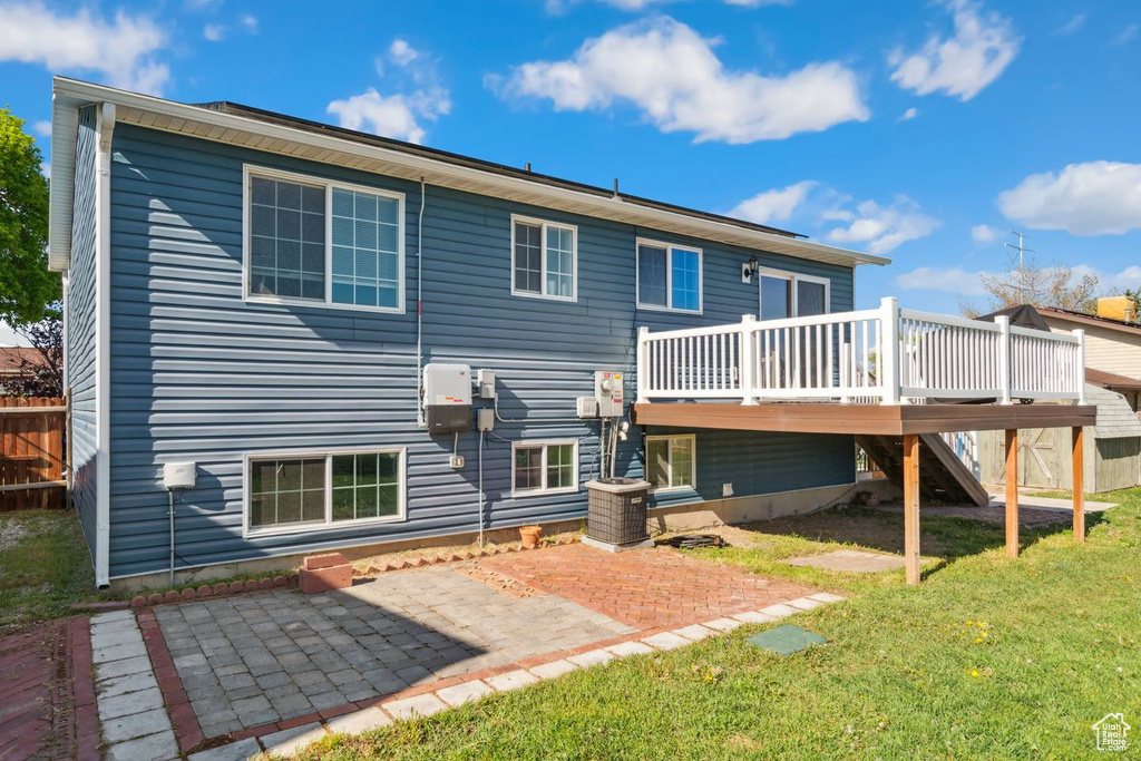 Back of property with a wooden deck, stairway, a lawn, a patio area, and central AC
