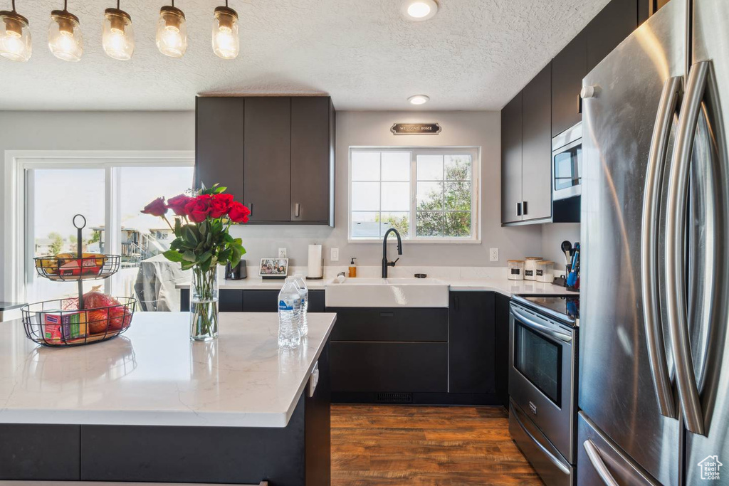 Kitchen with appliances with stainless steel finishes, a sink, a textured ceiling, dark wood-style flooring, and pendant lighting