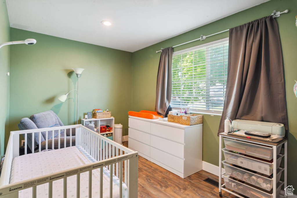 Bedroom featuring wood finished floors, a crib, recessed lighting, and baseboards