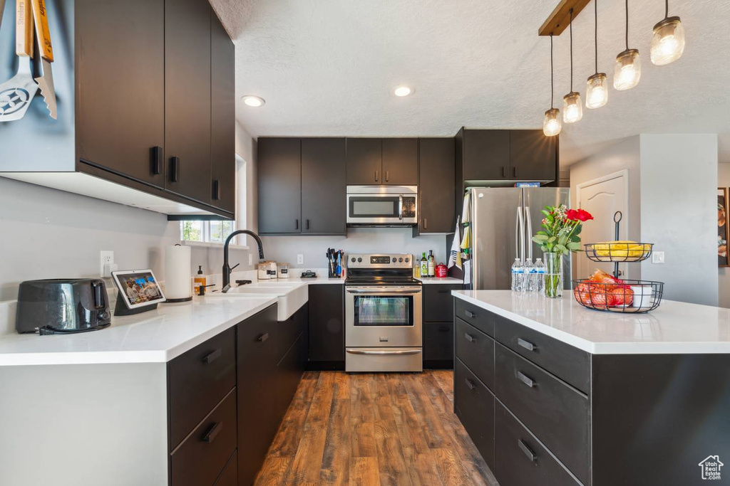 Kitchen featuring appliances with stainless steel finishes, a sink, dark wood-style flooring, pendant lighting, and light countertops