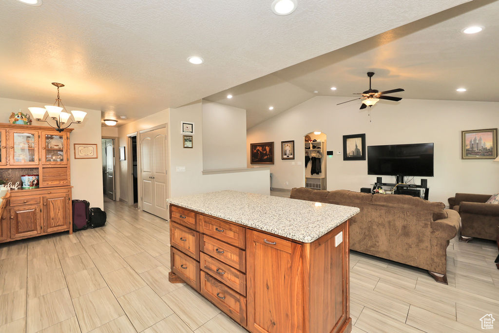 Kitchen with a chandelier, vaulted ceiling, a center island, a ceiling fan, and light stone counters