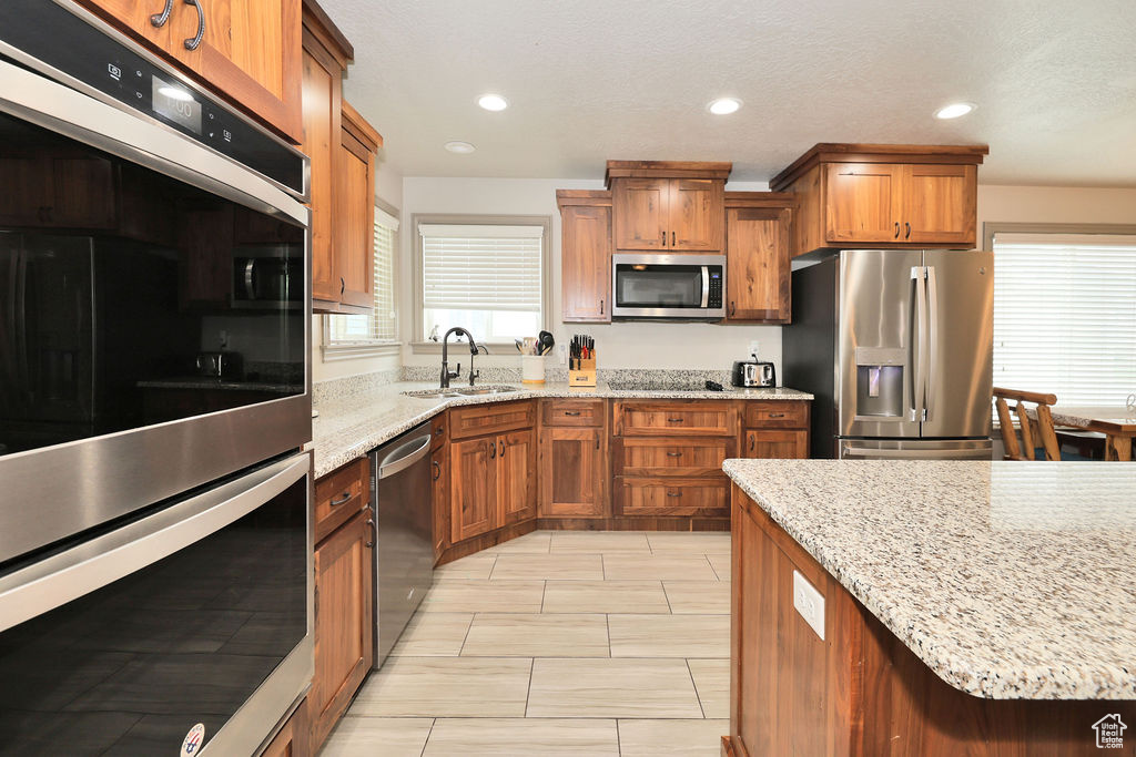 Kitchen featuring stainless steel appliances, a sink, brown cabinets, light stone countertops, and recessed lighting