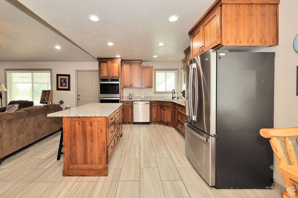 Kitchen with stainless steel appliances, open floor plan, brown cabinets, recessed lighting, and a sink
