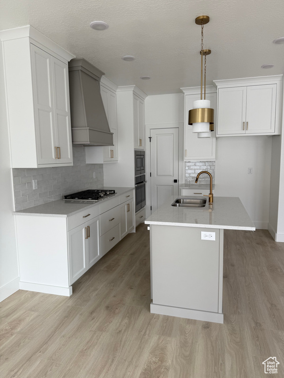 Kitchen featuring a sink, oven, wall chimney exhaust hood, light wood finished floors, and gas cooktop