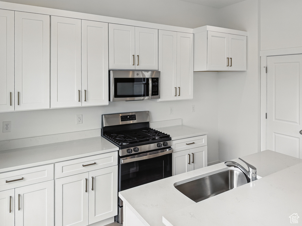 Kitchen with stainless steel appliances, a sink, white cabinetry, and light countertops