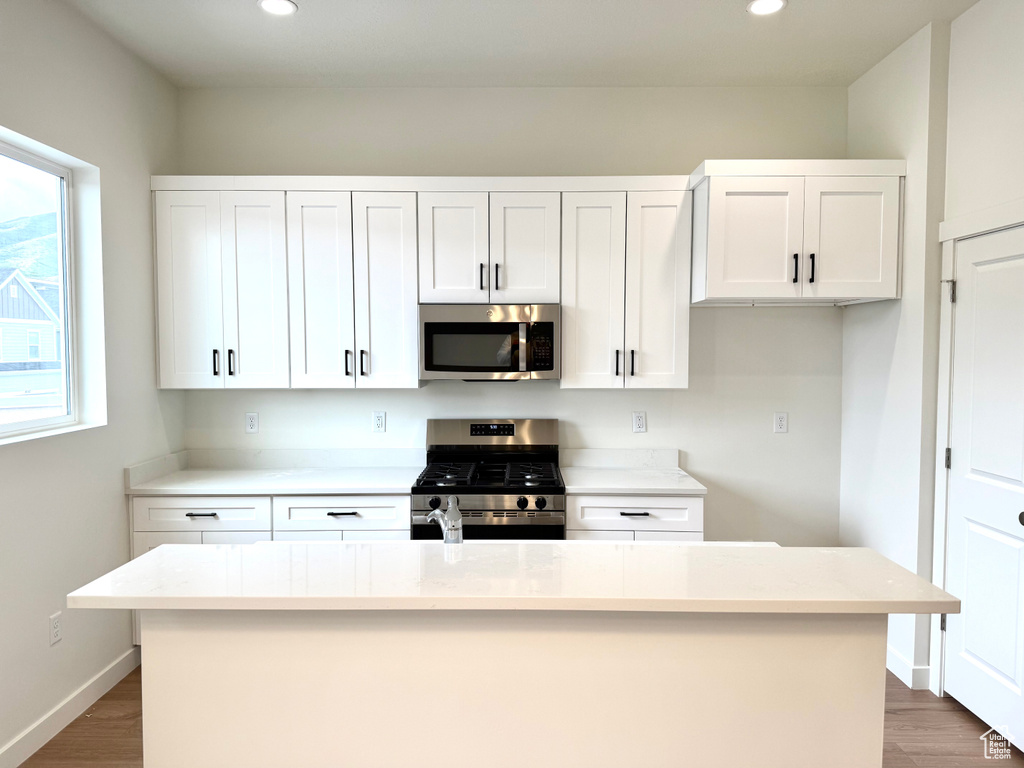 Kitchen featuring stainless steel appliances, recessed lighting, white cabinetry, light countertops, and a center island with sink