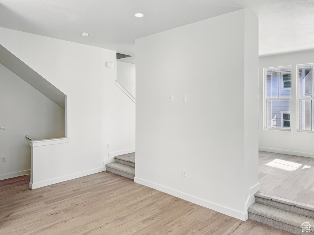 Unfurnished living room with stairs, light wood-type flooring, and baseboards