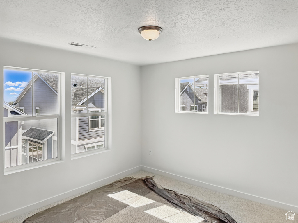 Carpeted empty room with a textured ceiling and baseboards