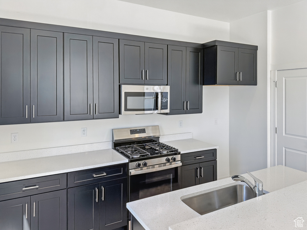 Kitchen with stainless steel appliances, a sink, and light stone countertops