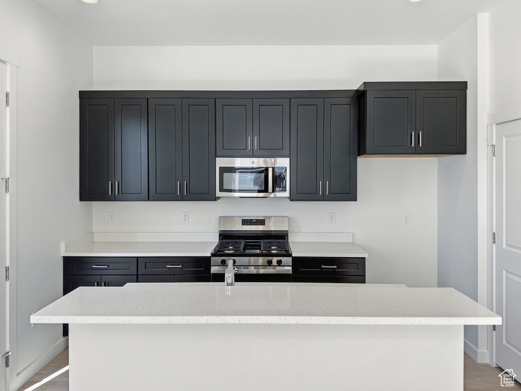 Kitchen featuring stainless steel appliances, baseboards, light stone countertops, and a center island with sink