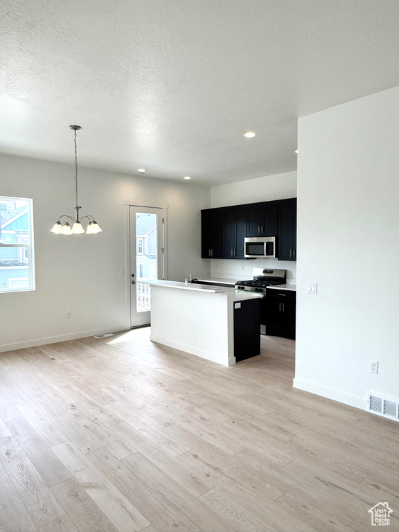 Kitchen with stainless steel appliances, dark cabinets, light wood-style flooring, open floor plan, and a textured ceiling