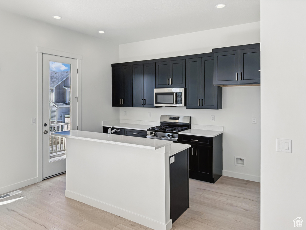 Kitchen featuring stainless steel appliances, light wood-style floors, baseboards, dark cabinetry, and recessed lighting