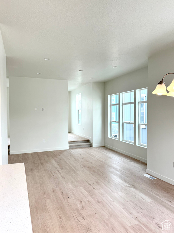 Unfurnished living room featuring light wood finished floors, baseboards, and a textured ceiling