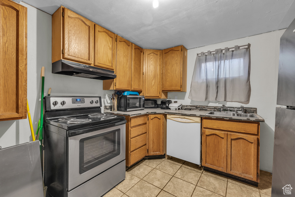 Kitchen with appliances with stainless steel finishes, under cabinet range hood, a sink, light tile patterned floors, and brown cabinets