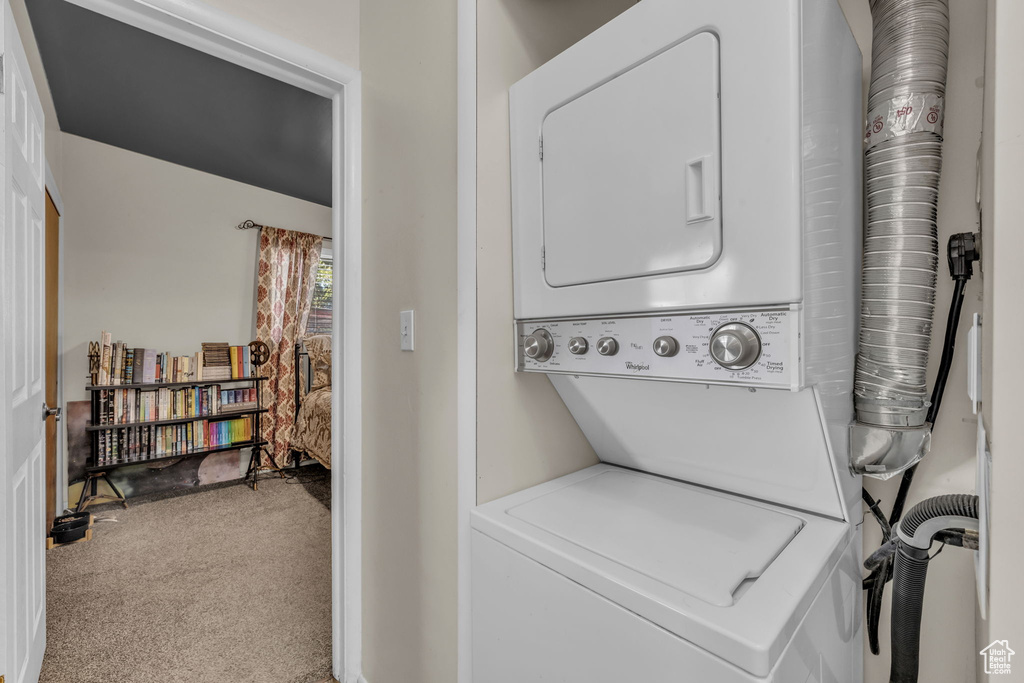 Washroom with stacked washer and clothes dryer and carpet