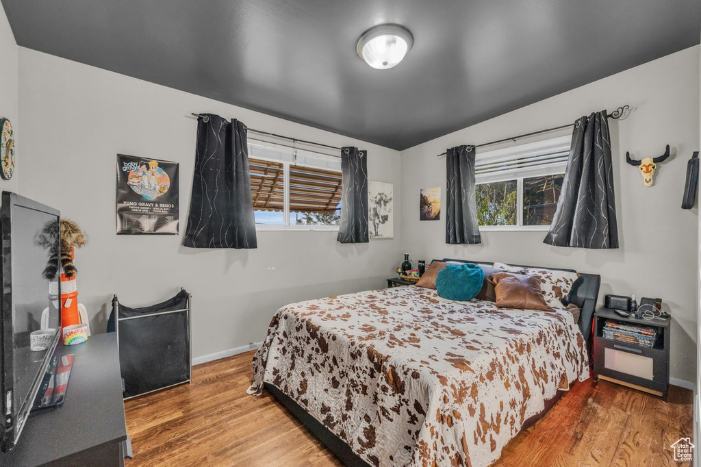Bedroom with wood finished floors, lofted ceiling, and baseboards