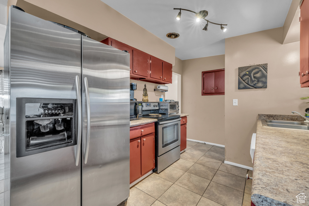 Kitchen with appliances with stainless steel finishes, light tile patterned flooring, a sink, and light countertops