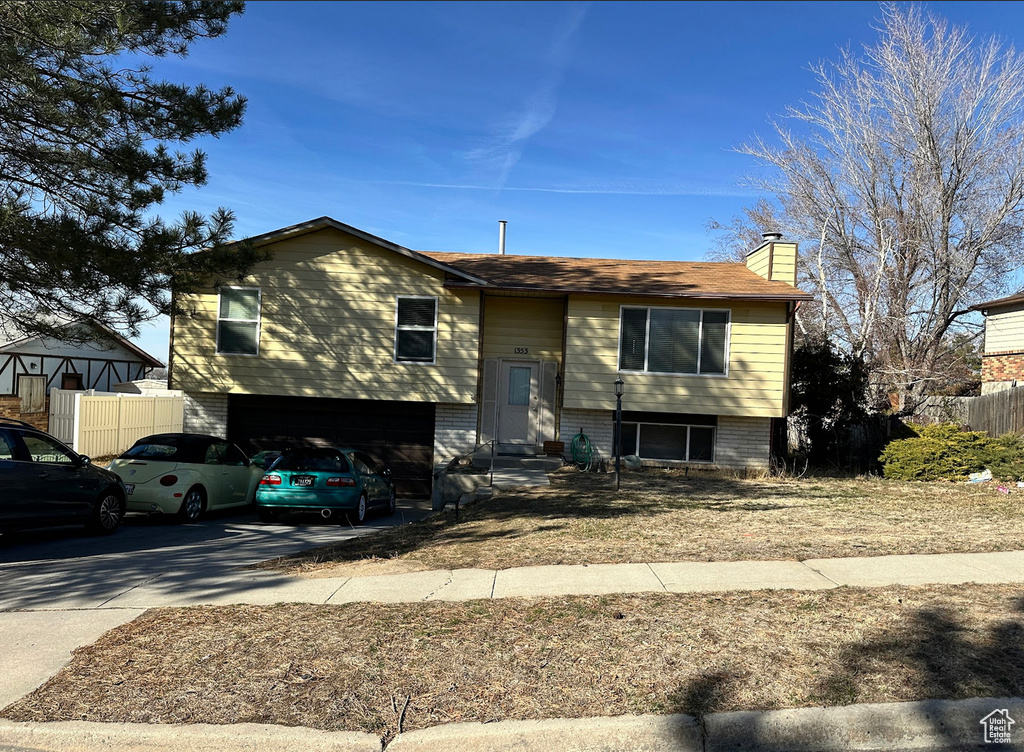 Split foyer home featuring a chimney, a garage, driveway, fence, and entry steps
