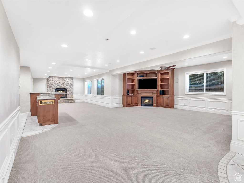 Unfurnished living room with a stone fireplace, a decorative wall, light colored carpet, recessed lighting, and wainscoting