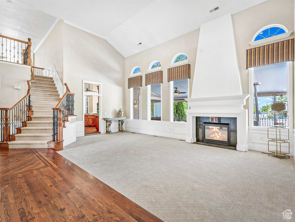 Unfurnished living room featuring high vaulted ceiling, stairway, a fireplace with flush hearth, carpet flooring, and wood finished floors