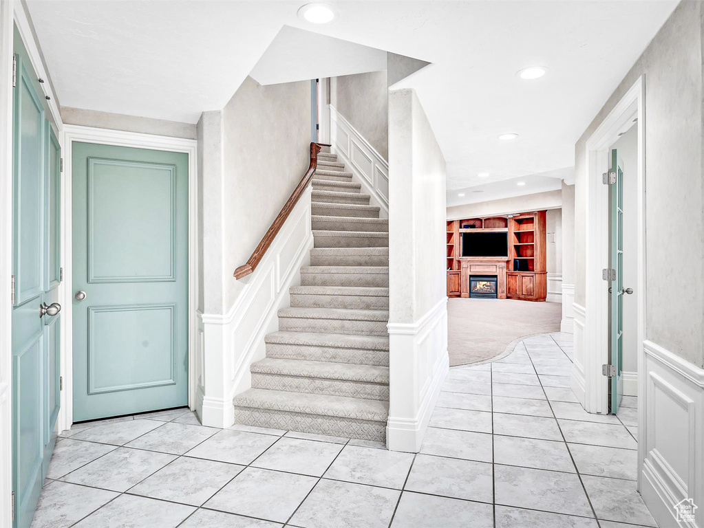 Stairway with a decorative wall, built in shelves, a glass covered fireplace, tile patterned flooring, and wainscoting