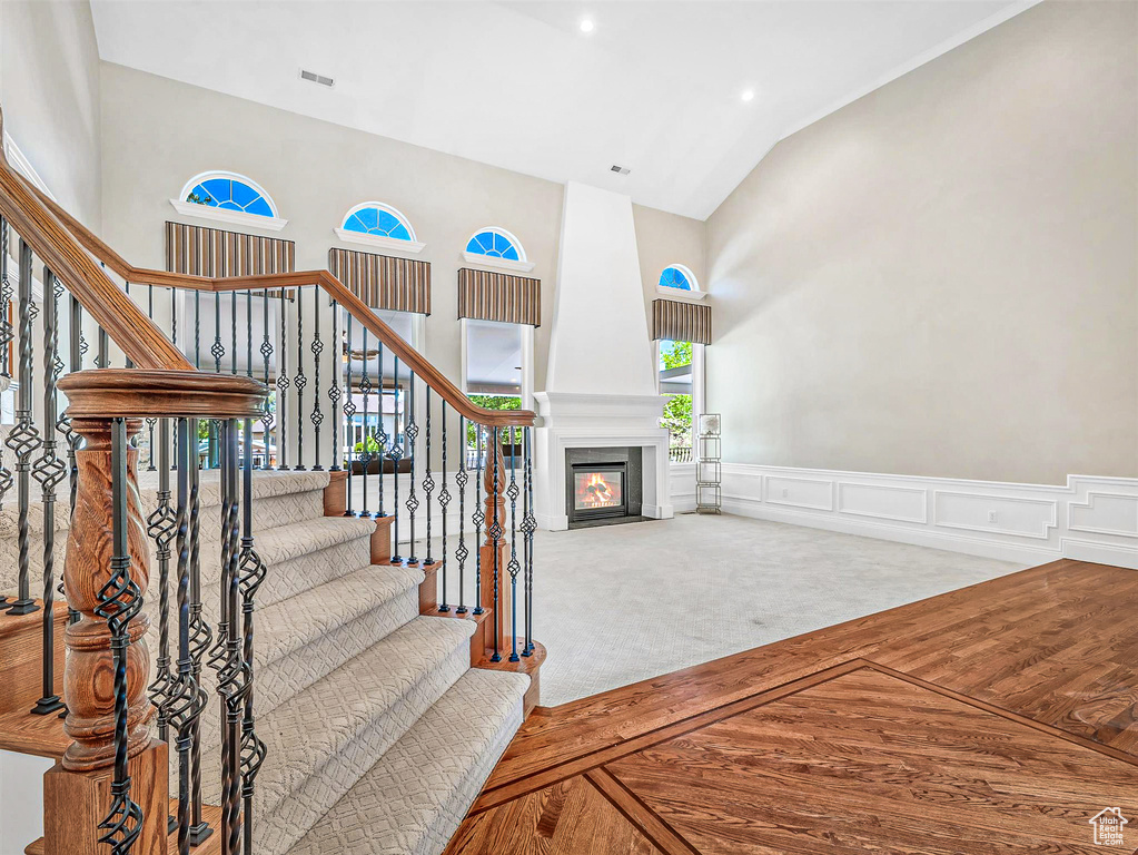 Staircase featuring high vaulted ceiling, a fireplace, wainscoting, a decorative wall, and carpet floors