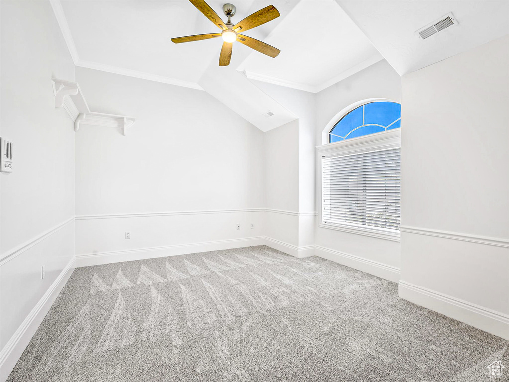 Carpeted empty room with a ceiling fan, ornamental molding, vaulted ceiling, and baseboards