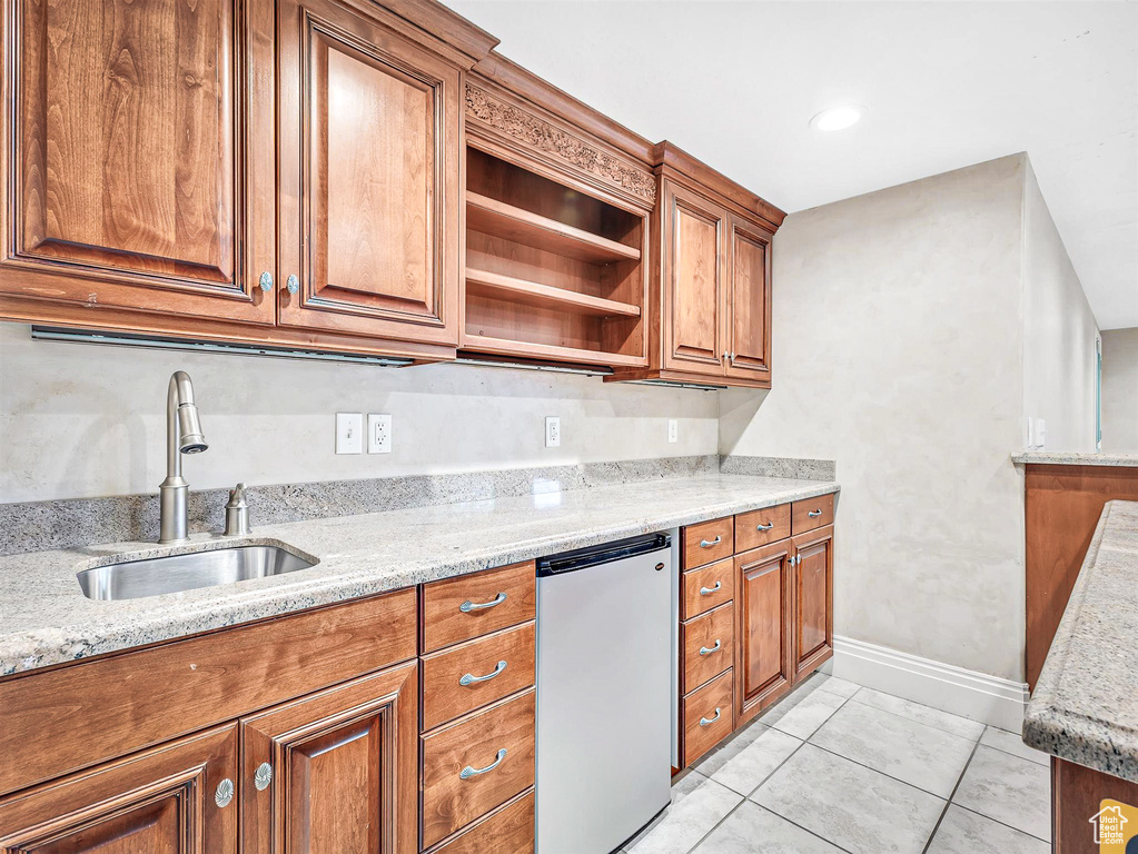 Kitchen with fridge, a sink, brown cabinets, light stone countertops, and baseboards