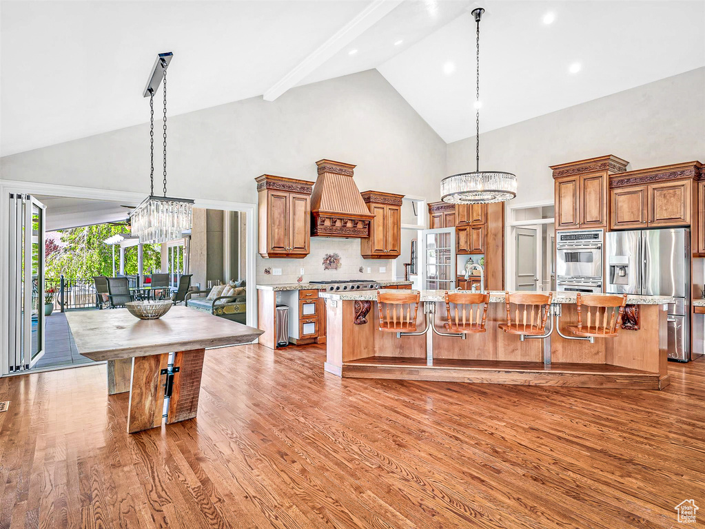 Kitchen with stainless steel appliances, high vaulted ceiling, a chandelier, custom range hood, and brown cabinets