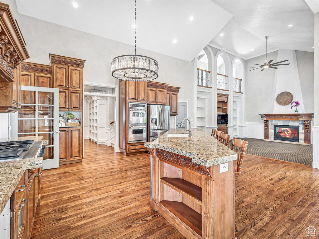 Kitchen featuring a high ceiling, a glass covered fireplace, a sink, open shelves, and appliances with stainless steel finishes