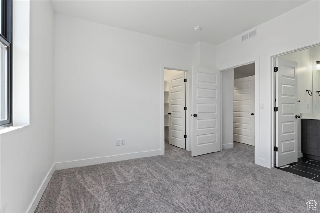 Unfurnished bedroom featuring carpet floors, baseboards, a walk in closet, and ensuite bath