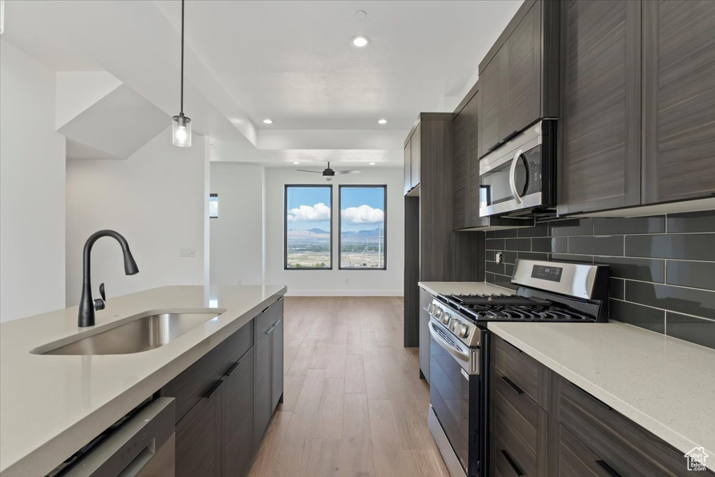 Kitchen with appliances with stainless steel finishes, a sink, decorative backsplash, light countertops, and light wood-type flooring
