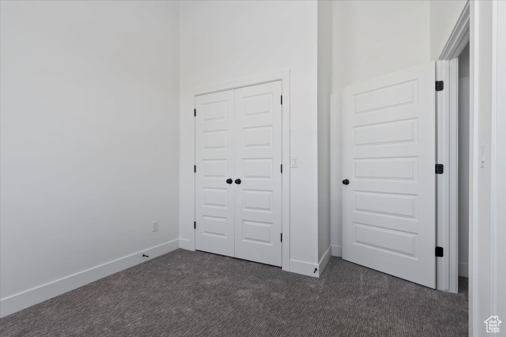 Unfurnished bedroom featuring dark colored carpet, baseboards, and a closet