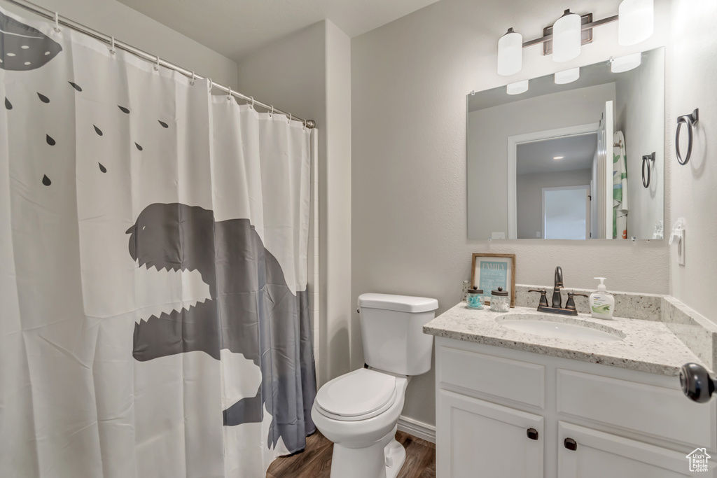 Bathroom featuring wood finished floors, toilet, vanity, baseboards, and a shower with shower curtain