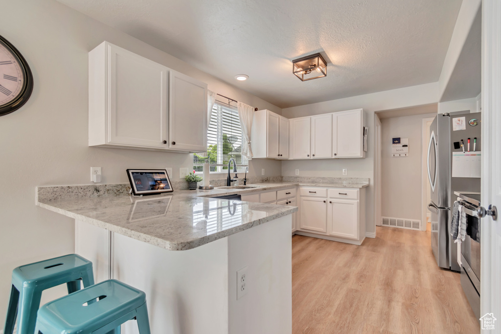 Kitchen with a peninsula, a sink, stainless steel appliances, white cabinets, and light wood finished floors