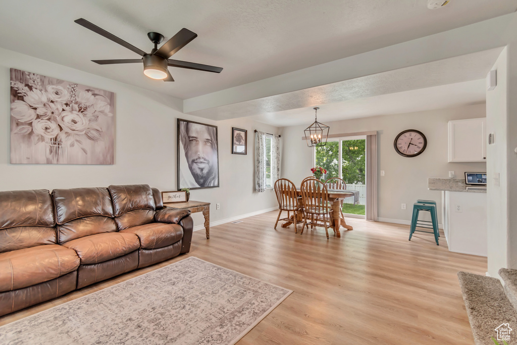 Living area featuring light wood-style flooring, baseboards, ceiling fan, and a chandelier